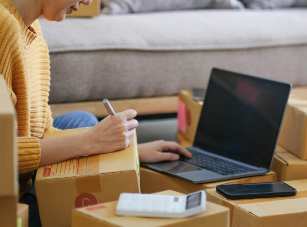 woman writing on cardboard boxes, woman typing on laptop, small business
