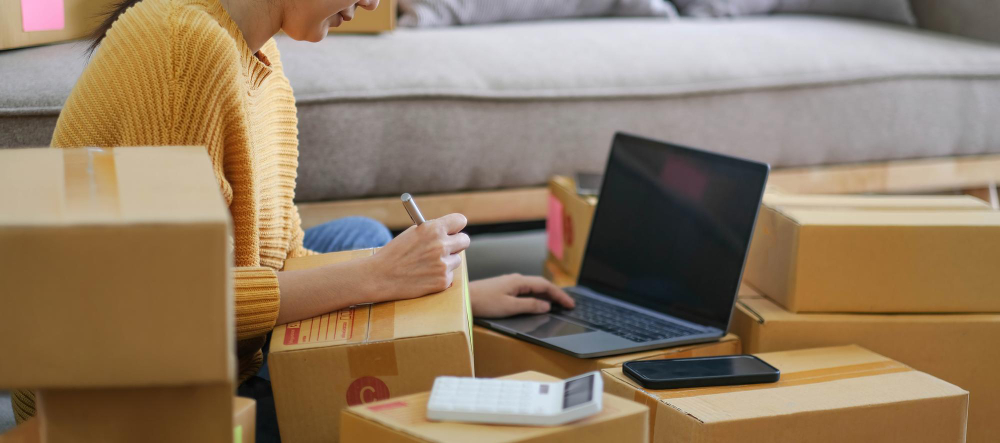 woman writing on cardboard boxes, woman typing on laptop, small business
